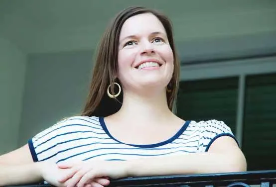 Valerie in her studio, warm candid portrait, waist-up with brushes and canvases.