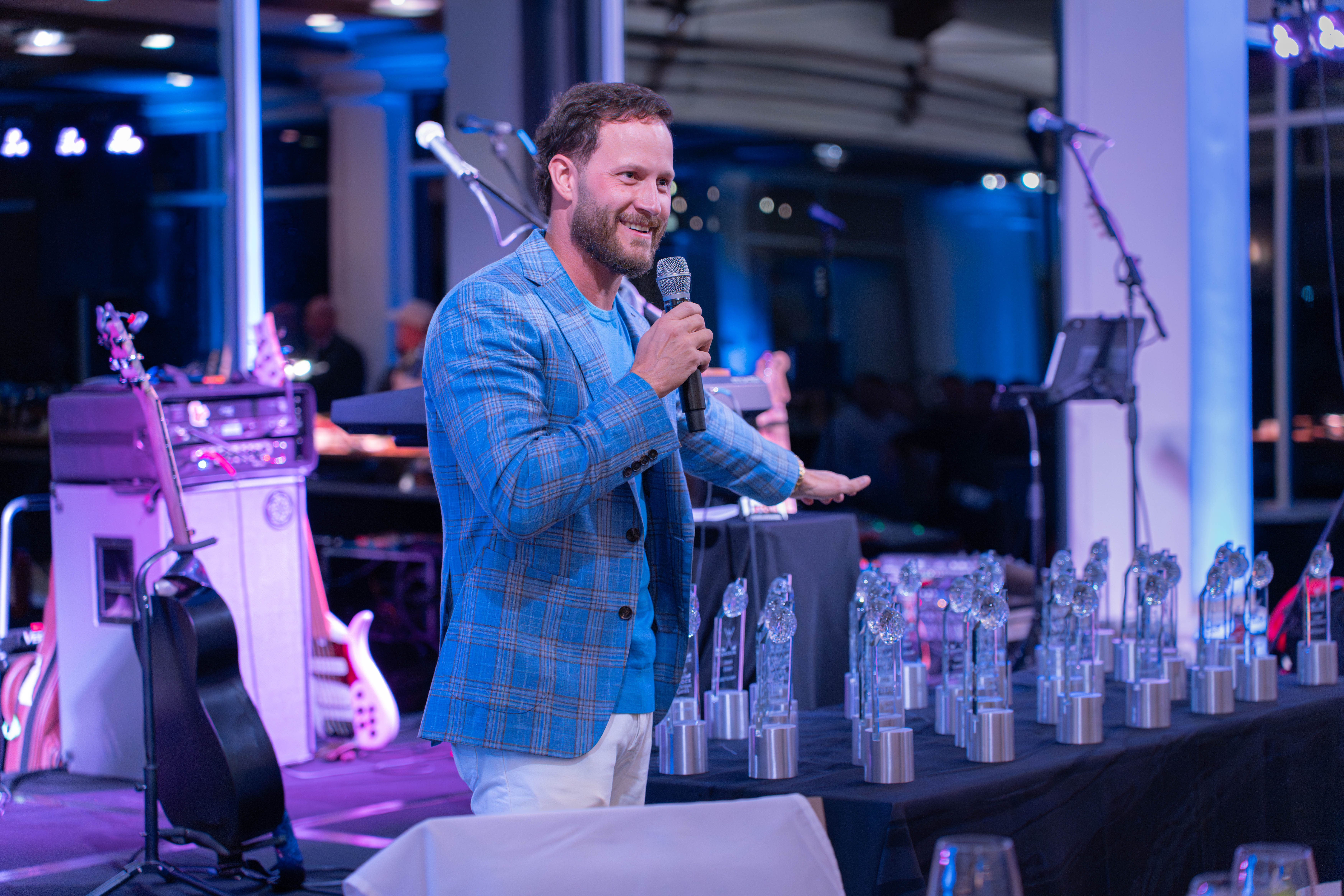 ustin Brock speaking at an event beside a table of awards while holding a microphone