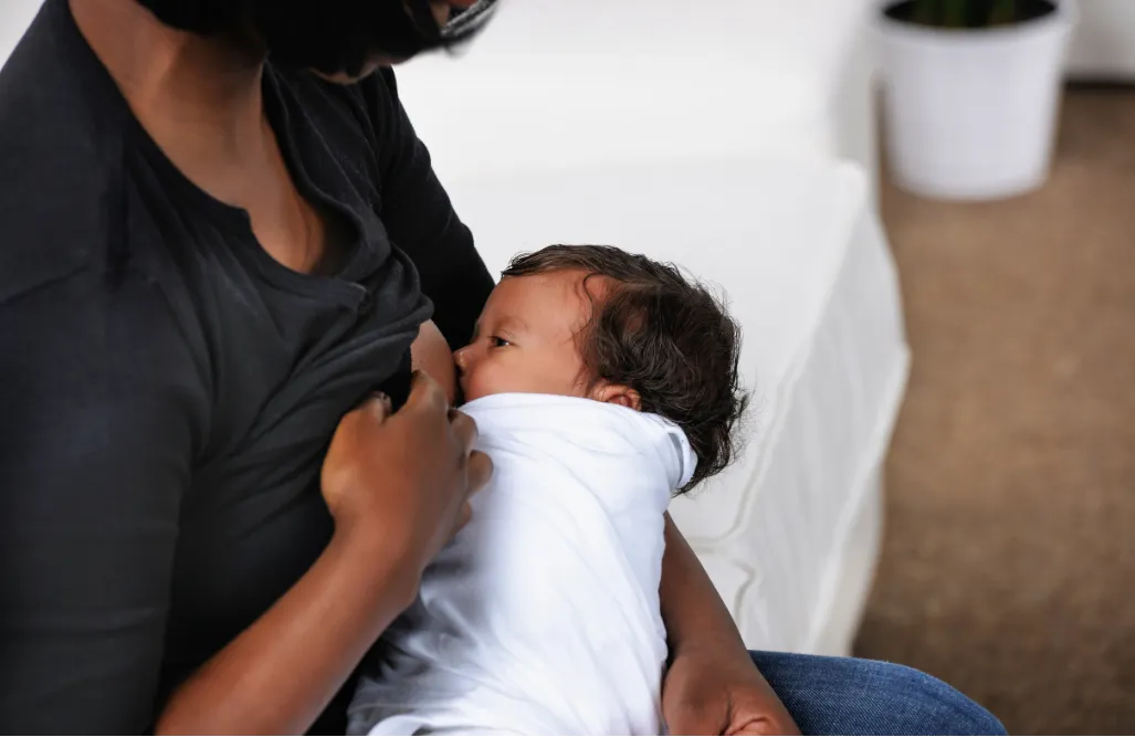 Mother breastfeeding her baby wrapped in a white blanket.