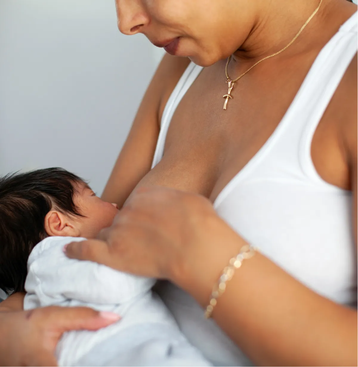 Person breastfeeding a baby, wearing a white tank top and gold necklace.