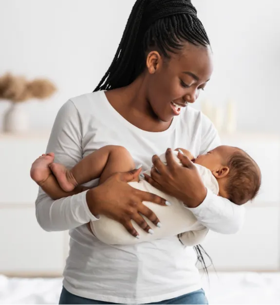 Smiling woman holding a baby in a cozy room.