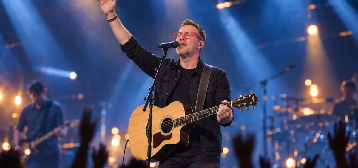 Man playing an acoustic guitar and singing on stage under warm spotlights.