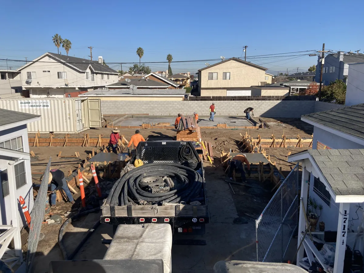Image shows a job site with a pump truck and eight finishers on top of large slabs finishing the concrete.