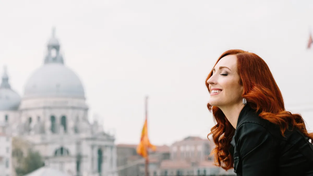 Allyson standing peacefully in Italy with orange flag in the background, embodying clarity and alignment during VIP Day coaching retreat