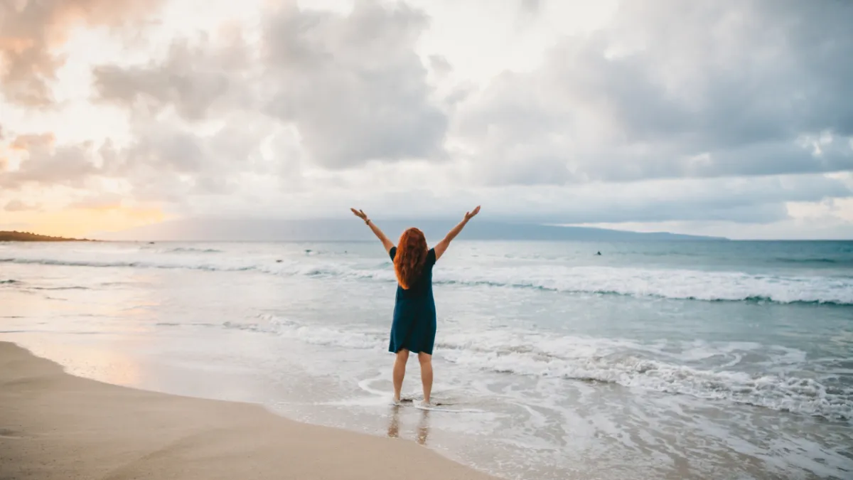 Allyson celebrating at the edge of the ocean in Hawaii with arms raised, symbolizing breakthrough and joy through 1:1 VIP coaching