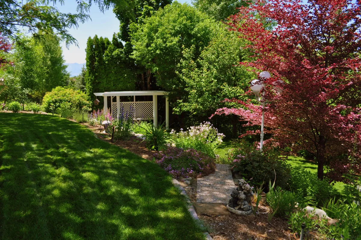 Image of outdoor garden landscape with trees mulch pavers rocks and flowers and shrubs and a gazeebo and a small trail