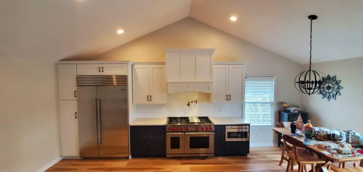 Kitchen and dining area with a vaulted ceiling, featuring modern stainless steel appliances, white cabinetry, and a wooden dining table under a stylish chandelier.