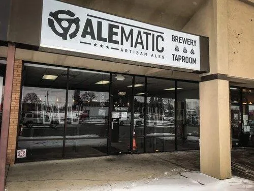 Front exterior of Alematic Brewery and Taproom in North Dayton, showcasing the modern industrial design with large glass windows and the Alematic Artisan Ales signage, created by Drake Architecture.