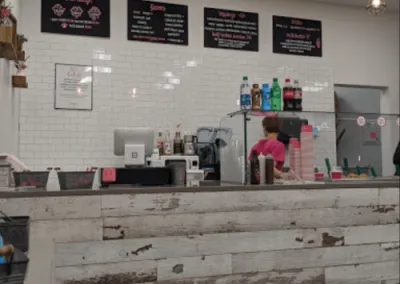 Close-up of the counter service area at No-Baked Cookie Dough shop, showcasing a rustic whitewashed wood counter, subway tile backsplash, and menu boards, all part of the modern design by Drake Architecture.