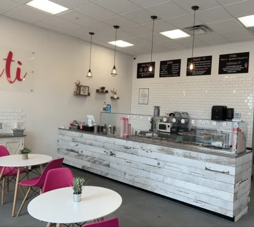 Interior view of No-Baked Cookie Dough shop, featuring a rustic counter with whitewashed wood, vibrant pink chairs, and a clean, modern design with menu boards overhead, created by Drake Architecture.