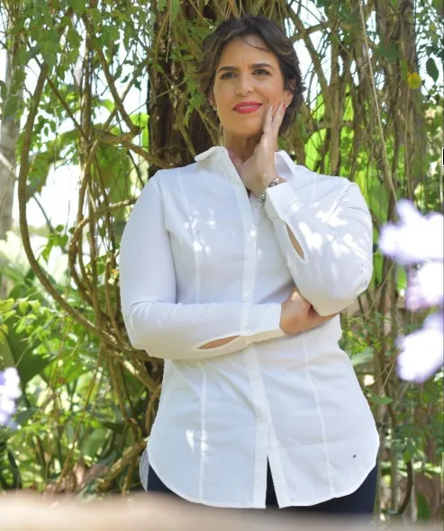 Mujer en calma, de pie frente a una ventana con luz cálida dorada, vistiendo tonos verde profundo y verde agua, con gesto de renacer y manos sobre el corazón. Fondo suave que integra los colores #F2C94C, #2F5D62 y #7BAE9E en un ambiente sereno.