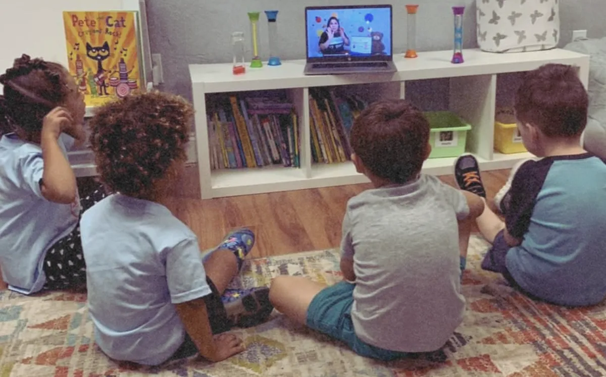 Students sit in a semicircle watching the teacher on a laptop