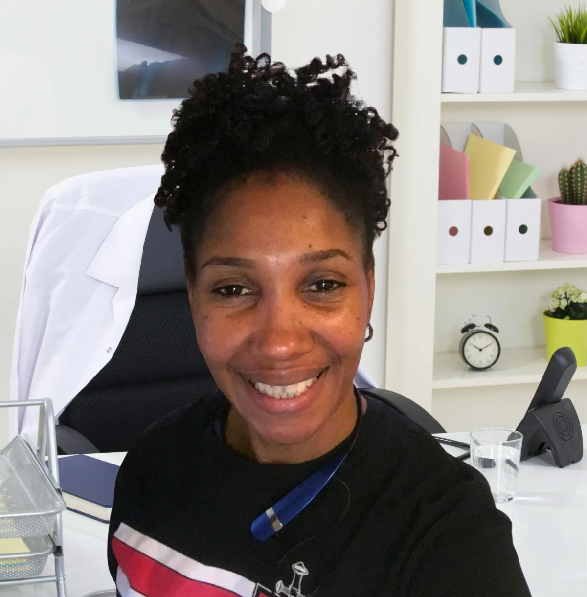 Portrait of the founder, an African American woman in her 40s, standing proudly in front of a family photo wall, wearing a navy blazer and a gentle smile. The background features framed family photos and soft, warm lighting.