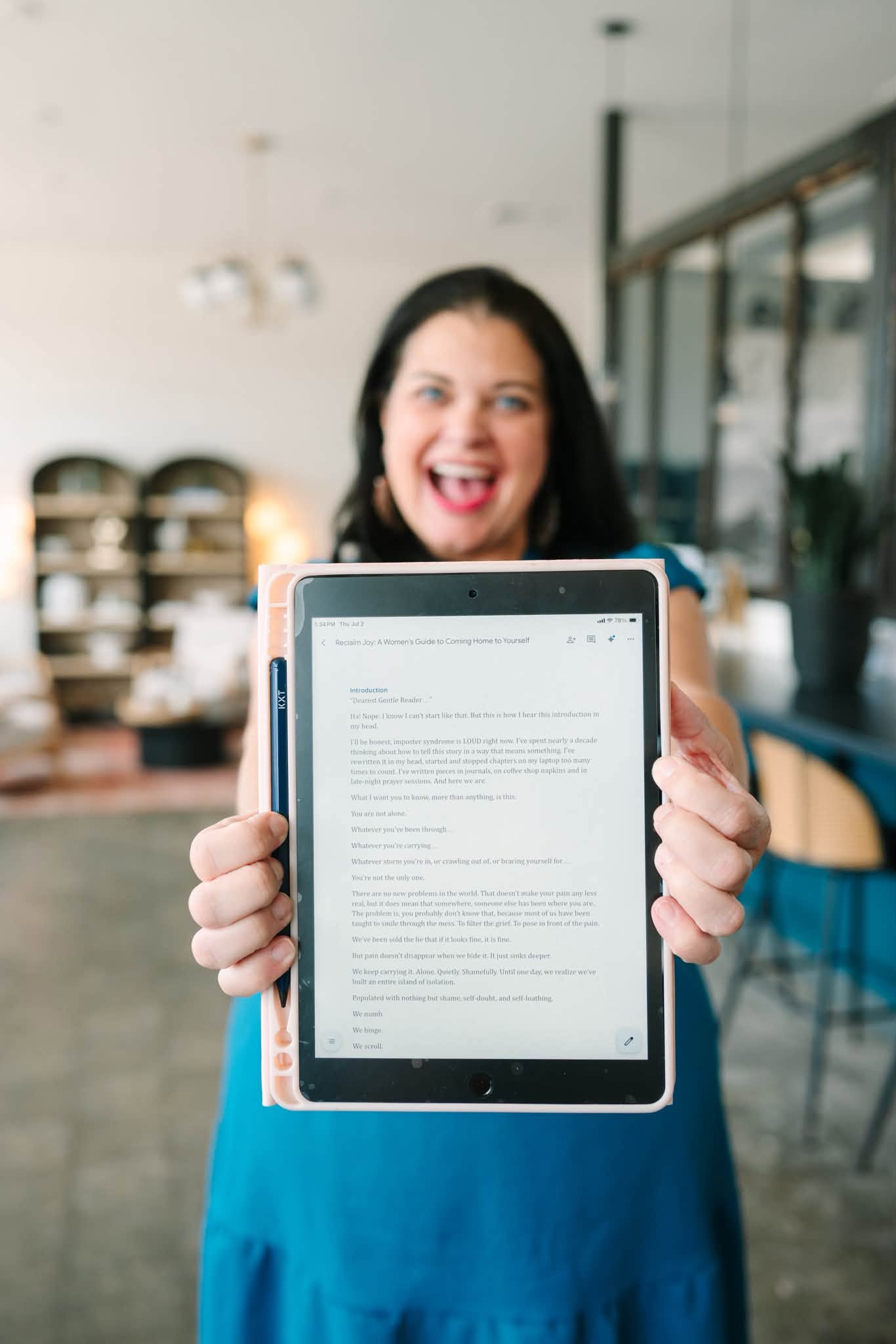 Blythe holds a screen with page one of her book Reclaim Joy: A Woman's Guide to Coming Home to Yourself on it