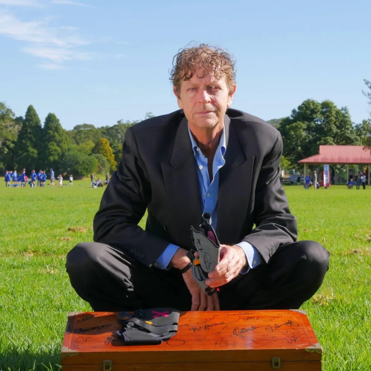 Craig J Hubbard holding a KiSS X Ankle Self-Rehab Safety System on a soccer field with soccer players playing soccer in the background