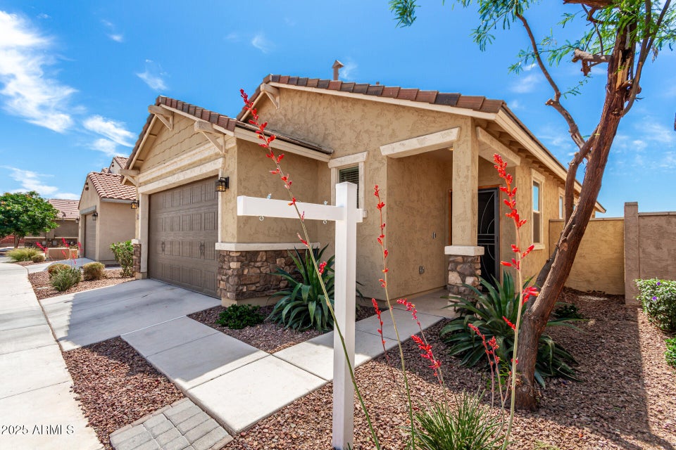 tan house with gravel and bushes out front 