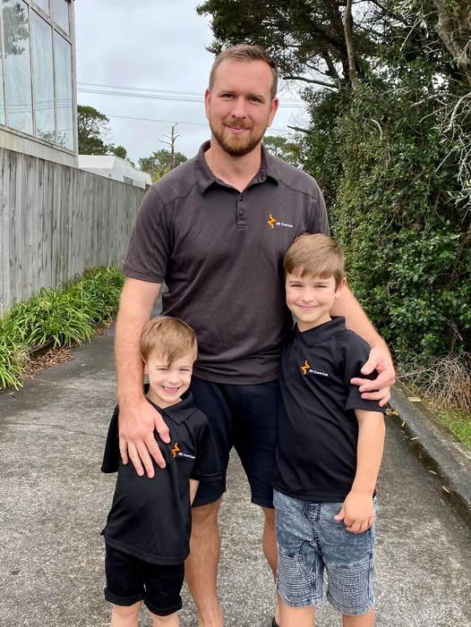 Zane from Zed Electrical Ltd standing with his two sons, wearing company uniforms on the North Shore, Auckland