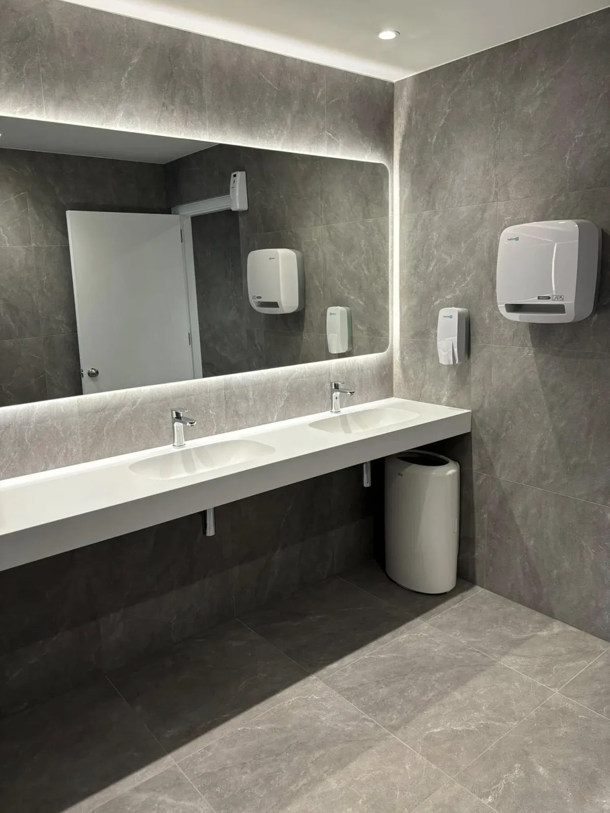 Modern commercial bathroom with LED backlit mirror and double sinks installed by Zed Electrical Ltd