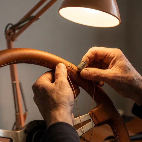 Expert automotive upholstery technician hand stitching a custom leather steering wheel showing premium craftsmanship and professional auto interior restoration work