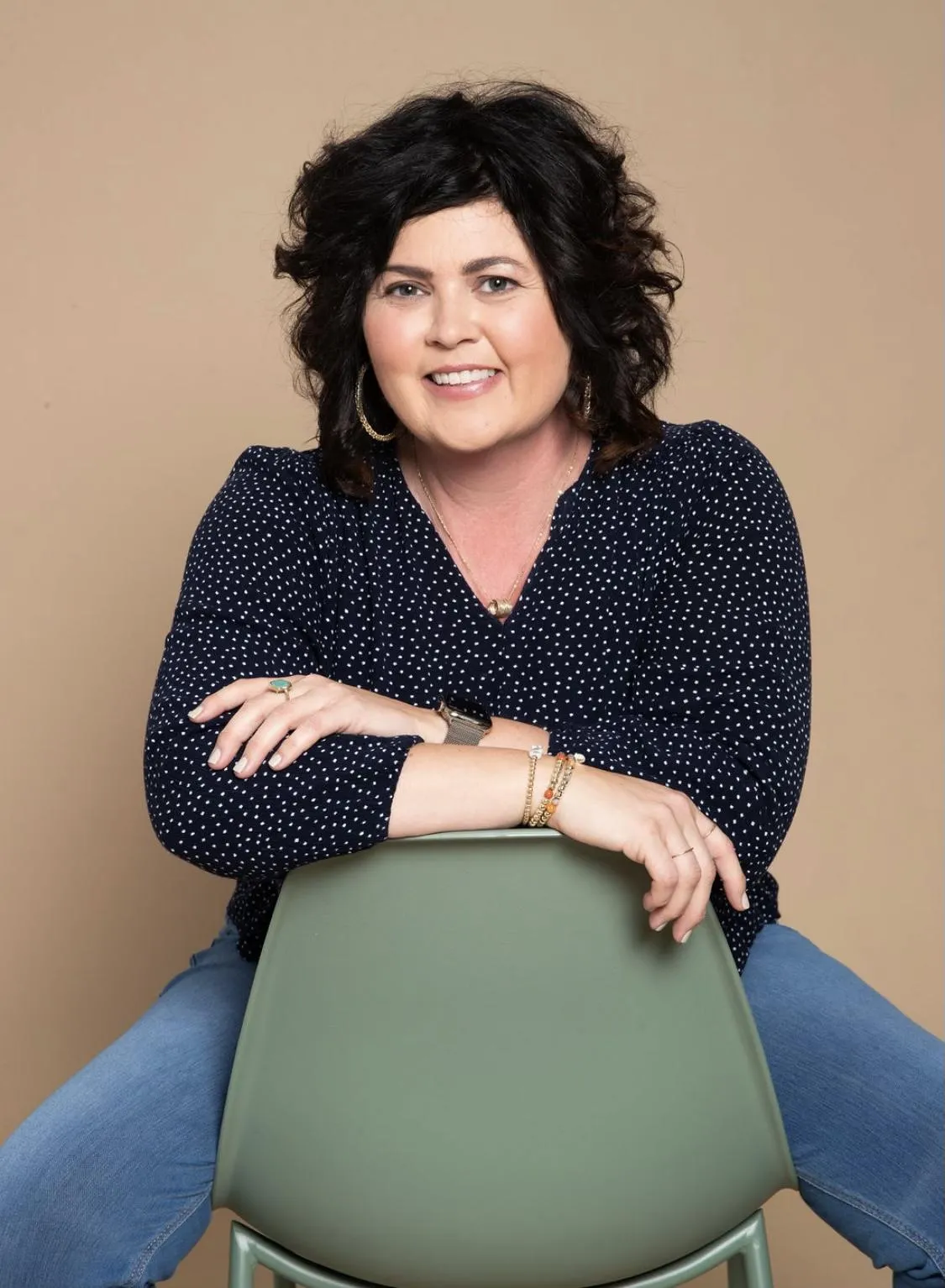 A woman in a green blouse rests her arm on a white surface