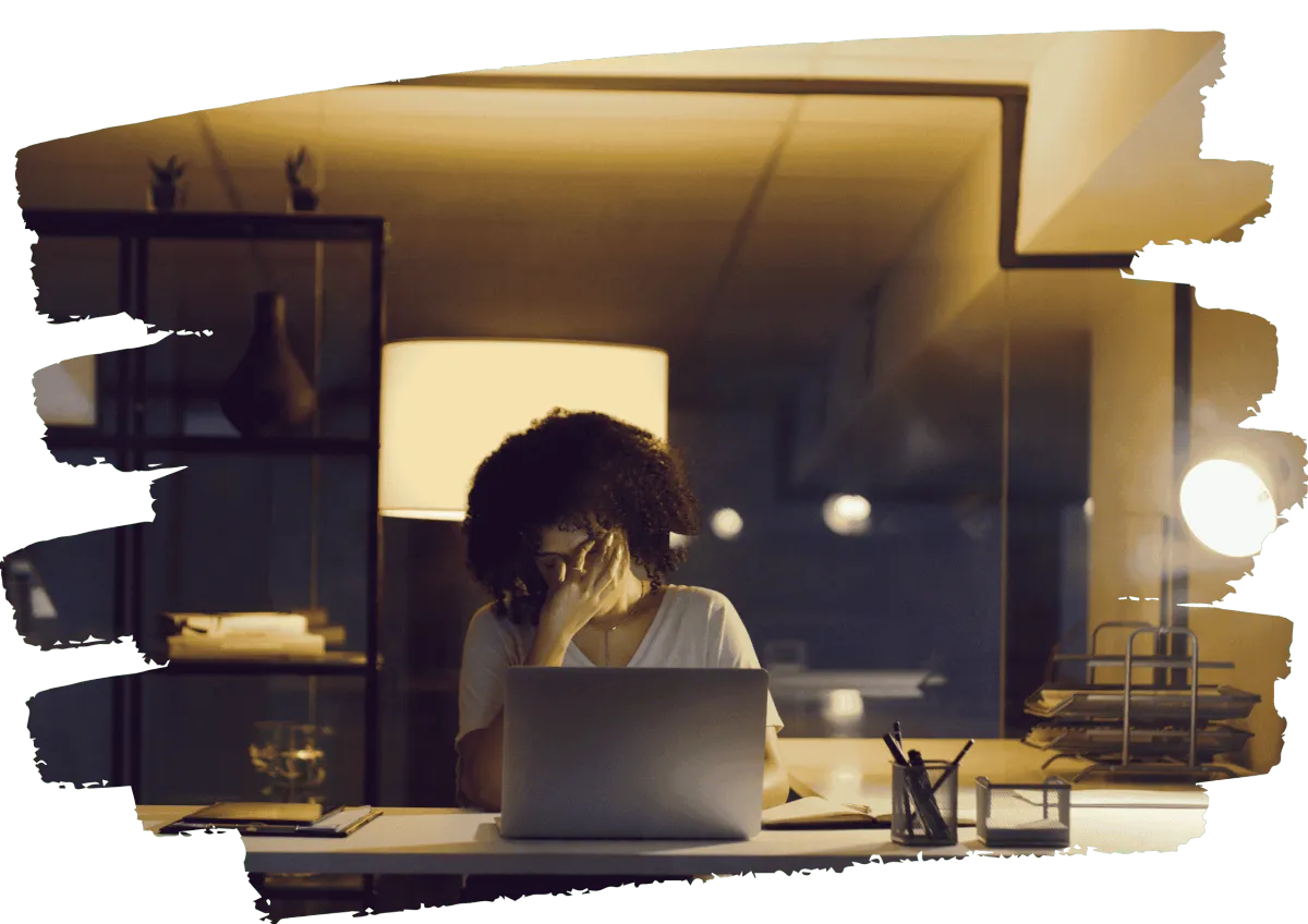 Woman sitting alone at desk at night feeling overwhelmed and unseen while working on laptop 