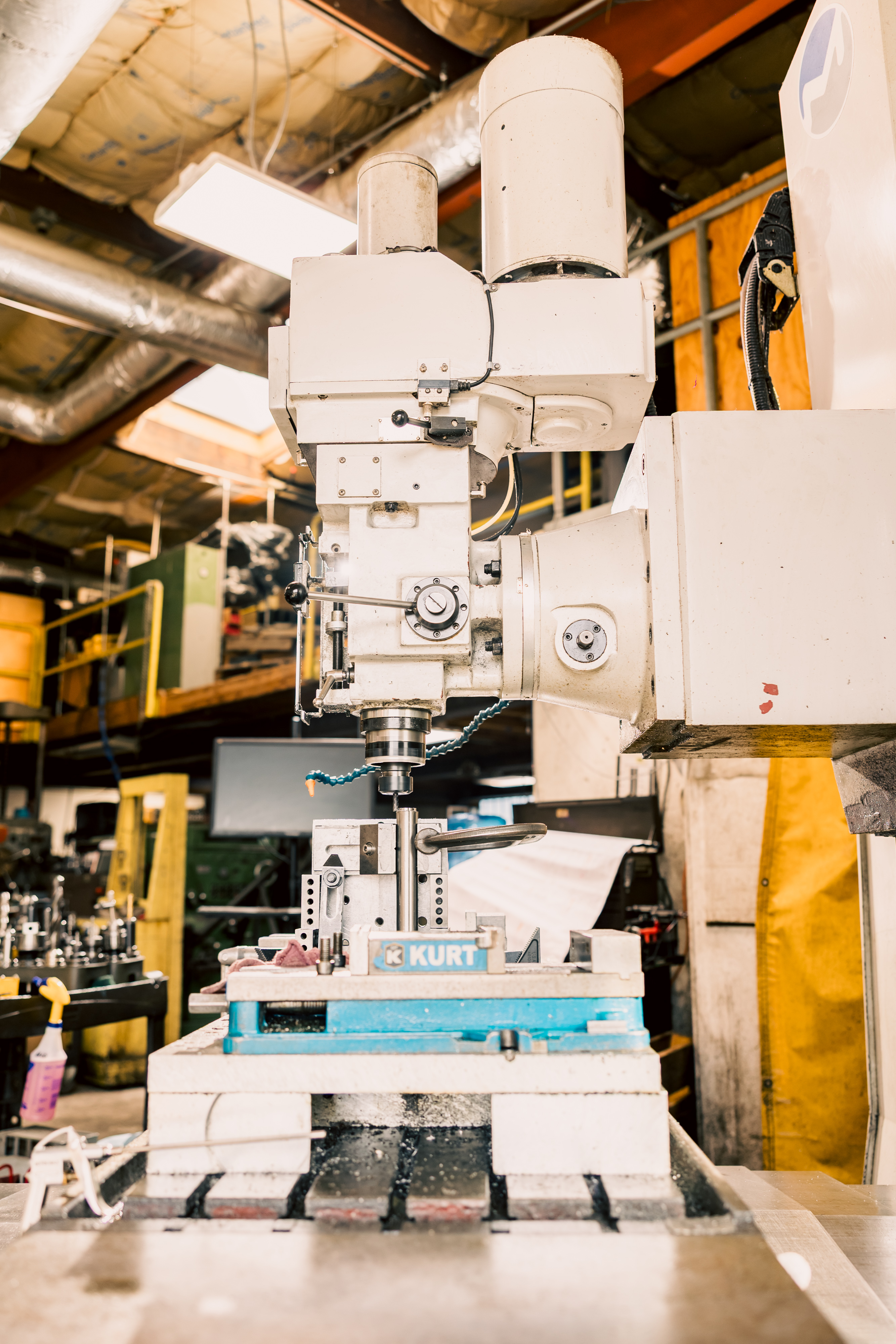 A white Milltronics MB30 toolroom bedmill with a Kurt vise in an industrial workshop setting.