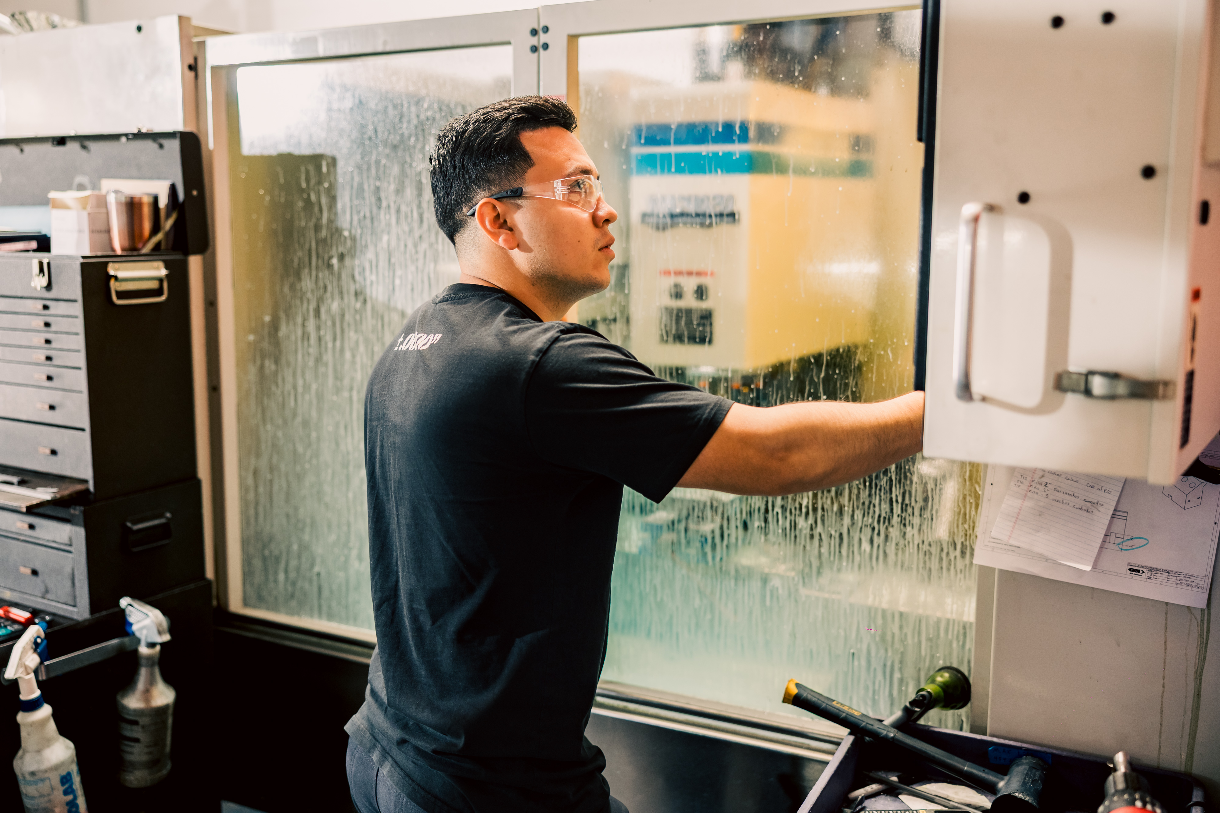 Miguel is operating a vertical machining center for precision CNC production in a workshop.