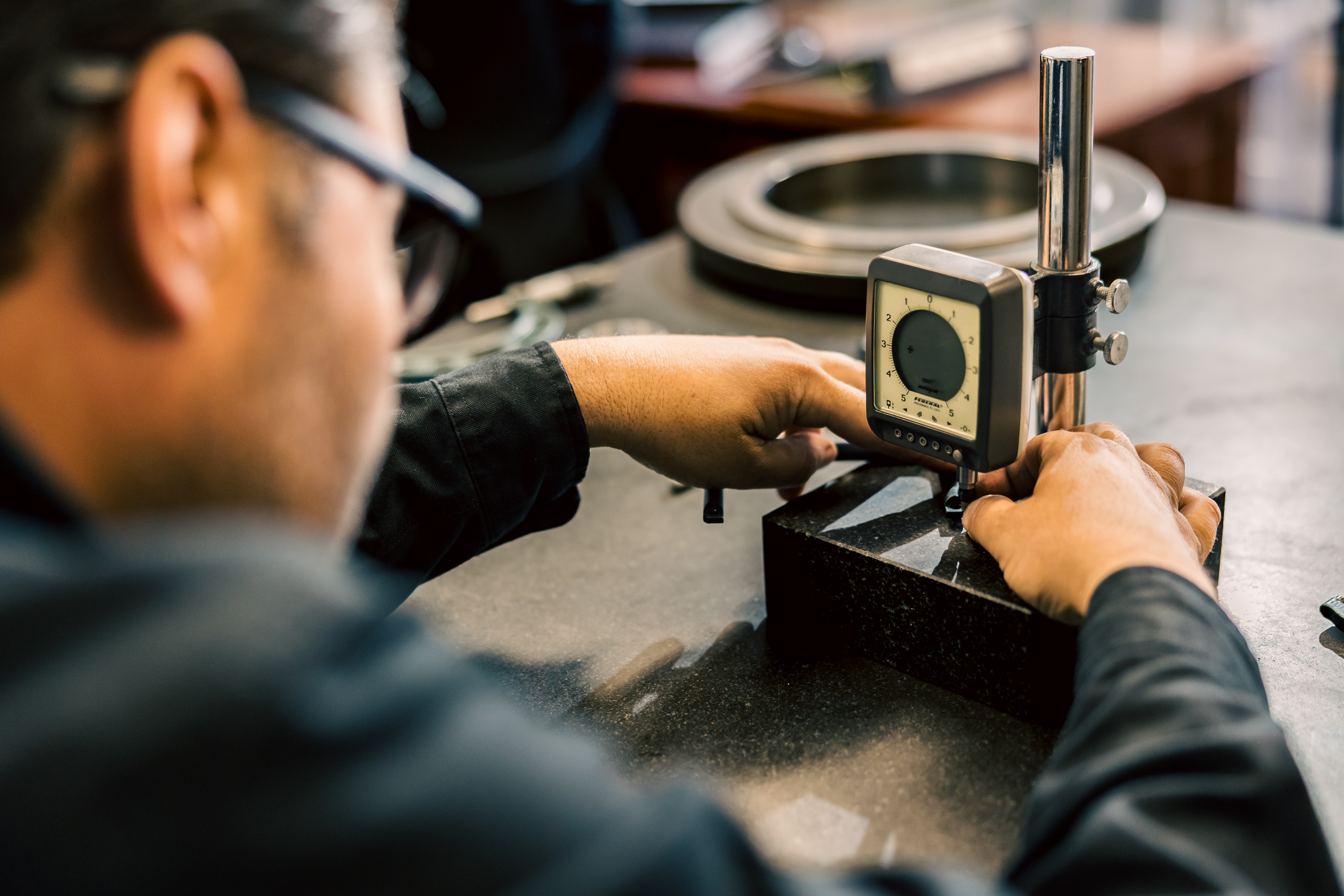 A close-up of a technician performing precision inspection on a machined component using a calibrated dial indicator at MTM.