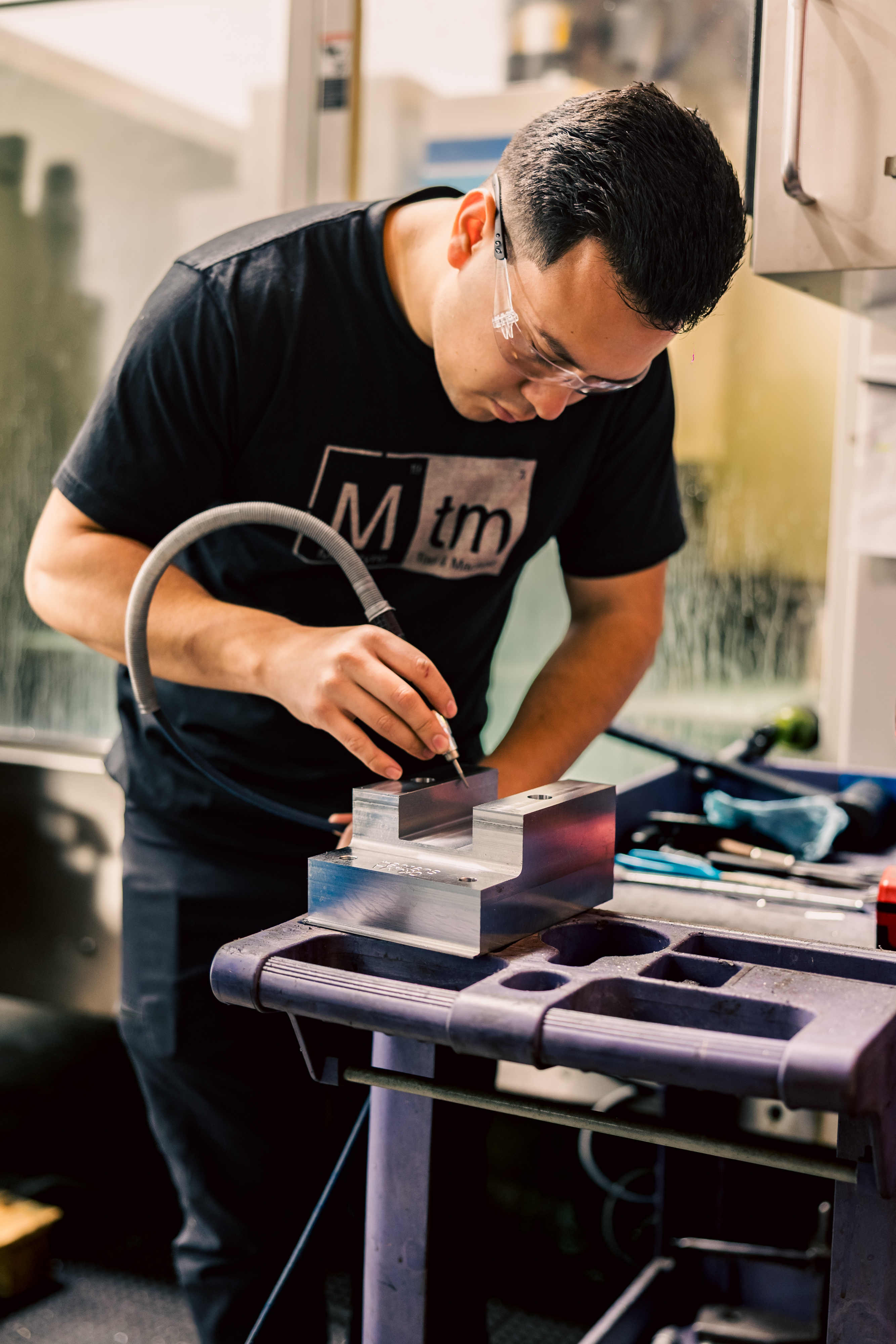 A machinist deburring a large metal block with a handheld high-speed rotary tool.
