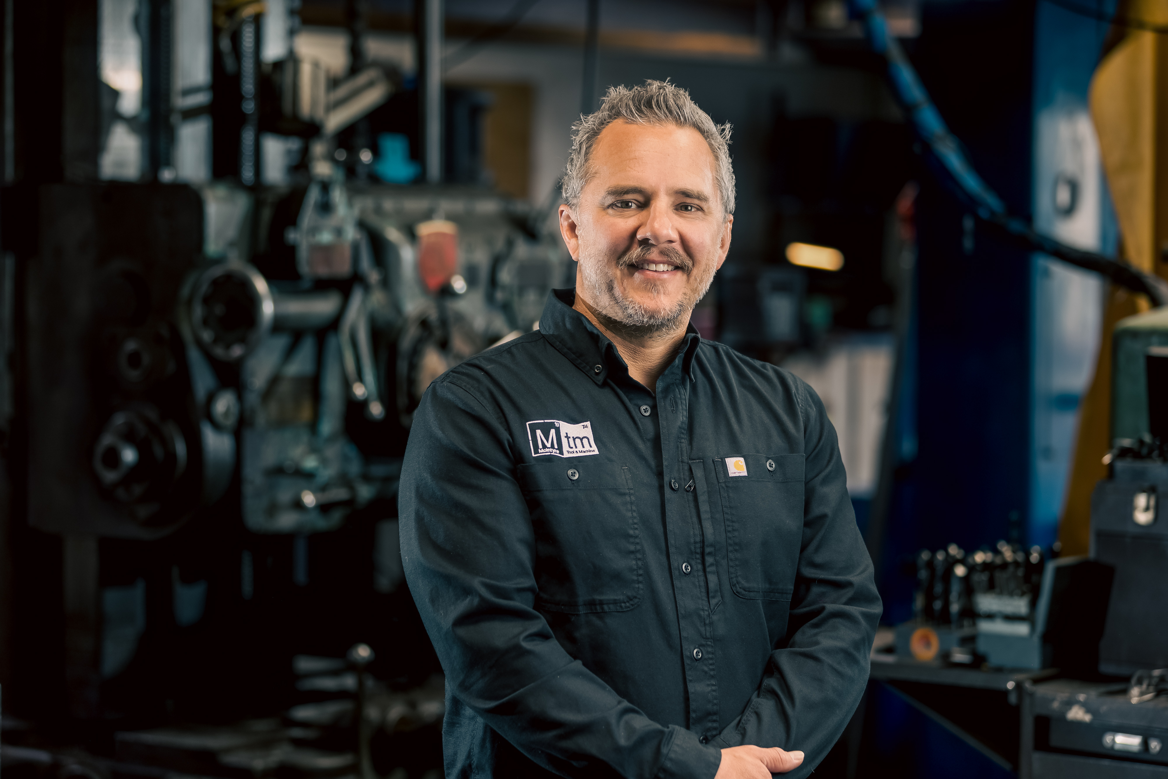A professional portrait of Dustin McIntyre, President of McIntyre Tool & Machine, smiling in his workshop.