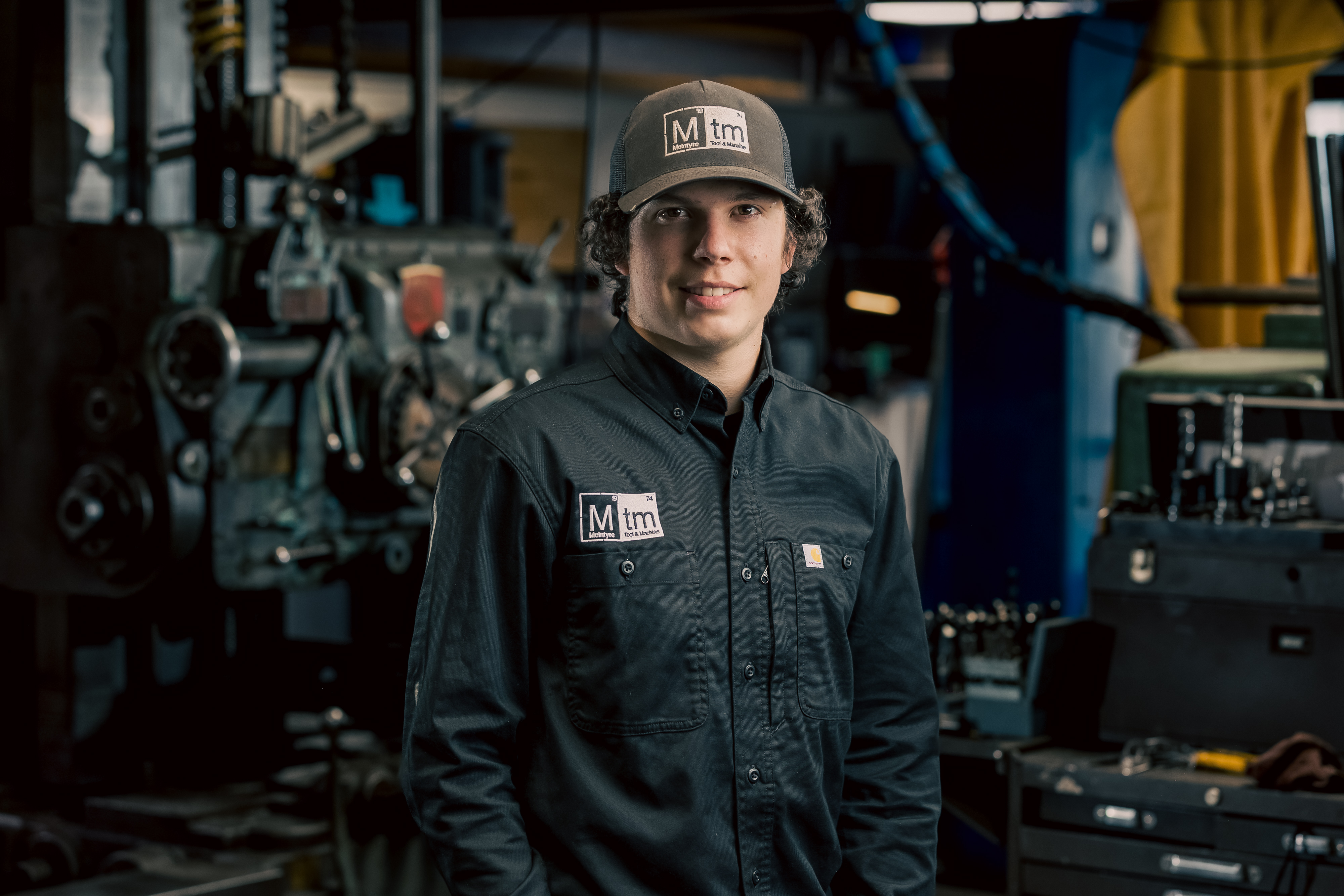 A professional portrait of Noah, a Production Assistant at MTM, wearing a black shirt and grey cap.