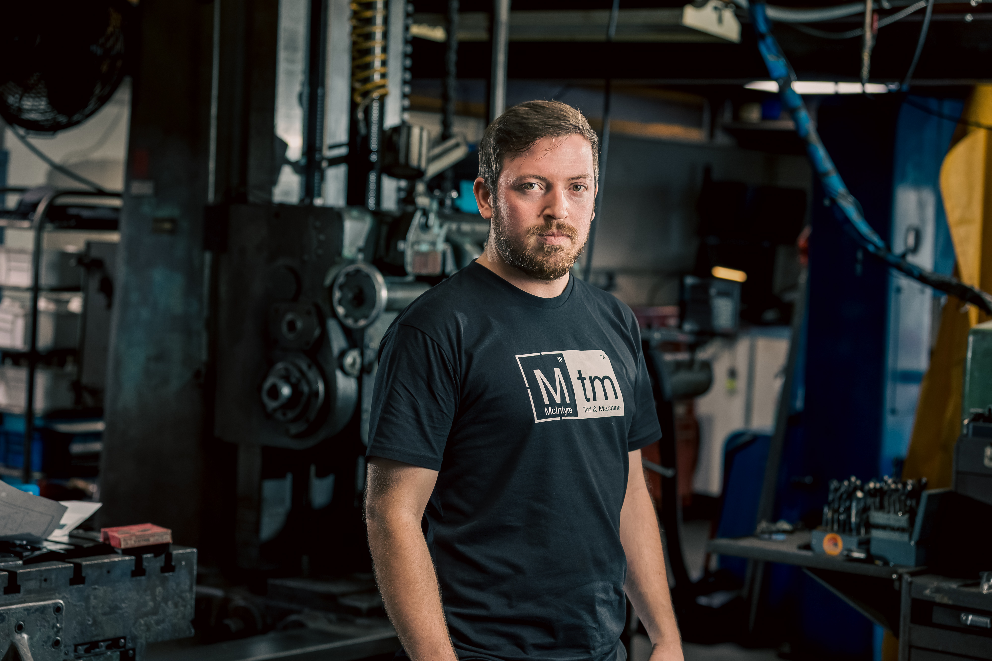A professional portrait of Nathan Deyling, Lead Fabricator at MTM, in his workshop wearing a black MTM shirt.