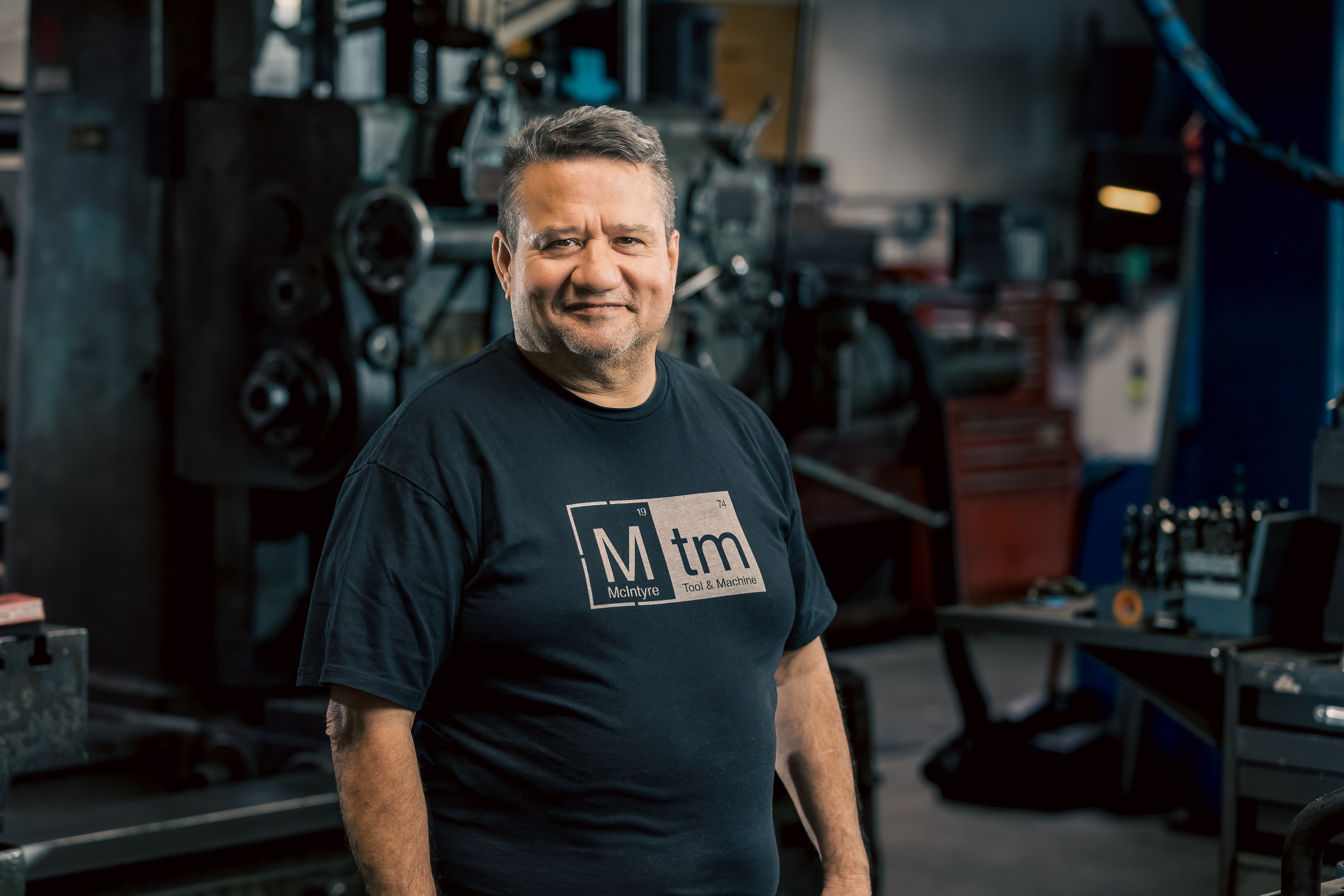 A professional portrait of Eulalio, a Tooling department Machinist at MTM, smiling in a black shirt.