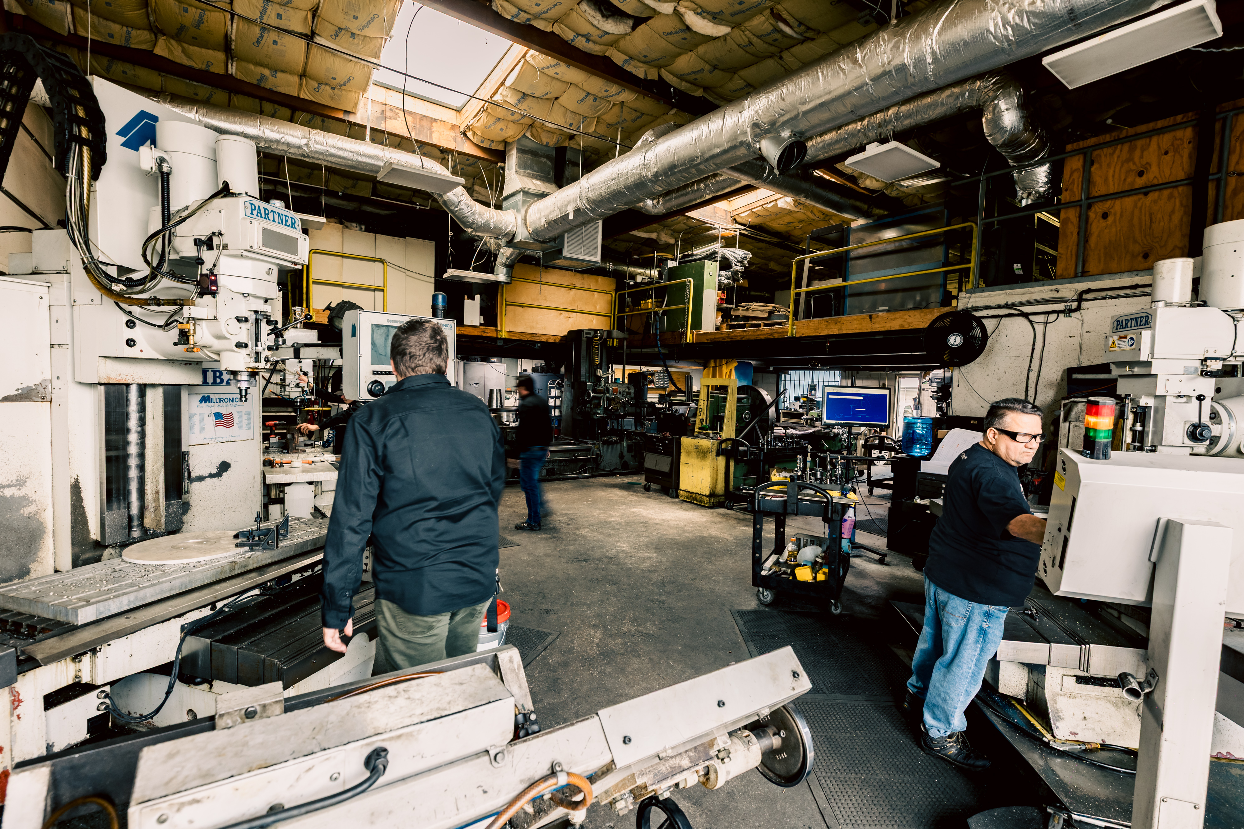 A wide interior shot of the Toolmaking Department with machinists working at large industrial machines.