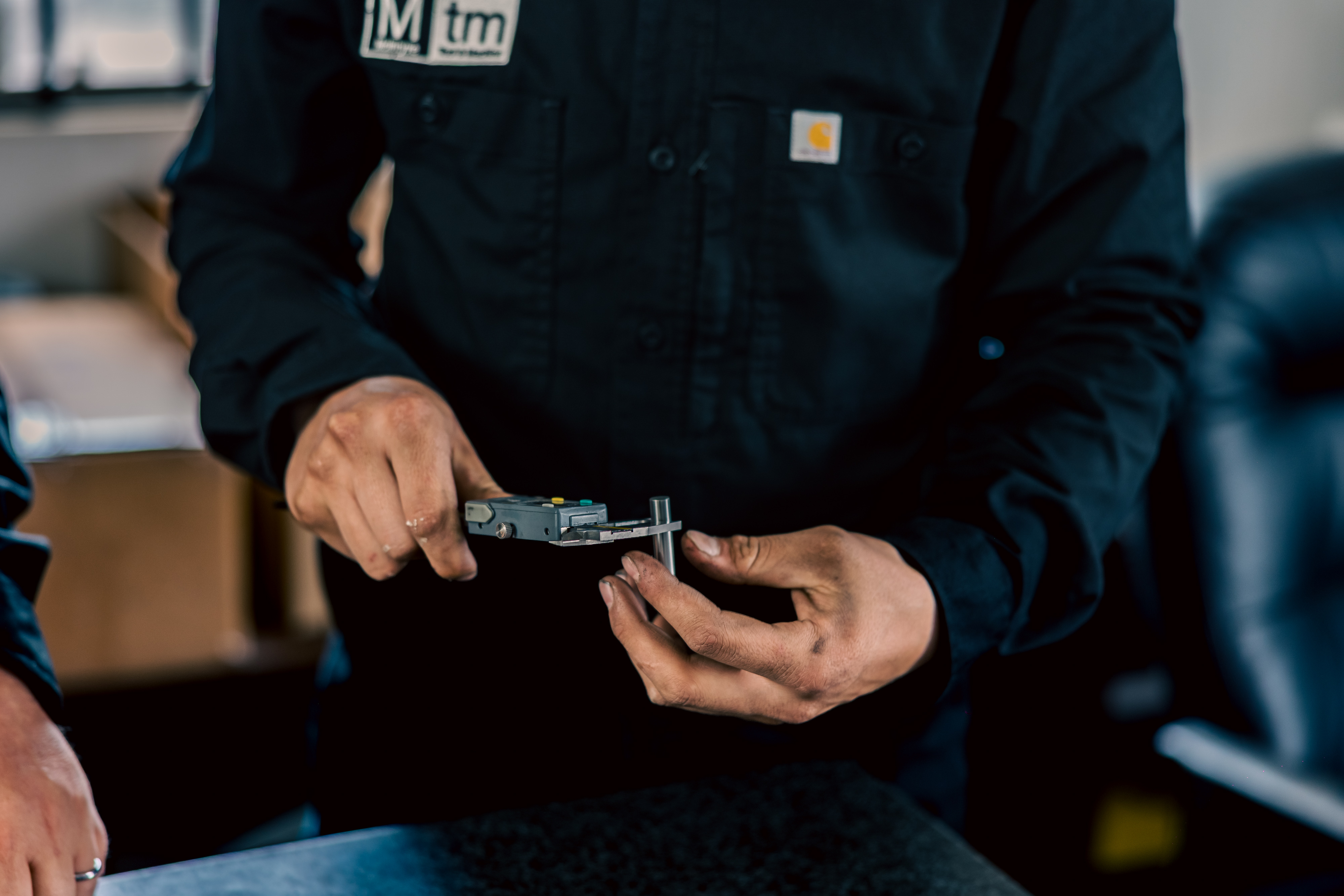 Noah is using digital calipers to inspect a small metal pin component at the assembly stage in the workshop.