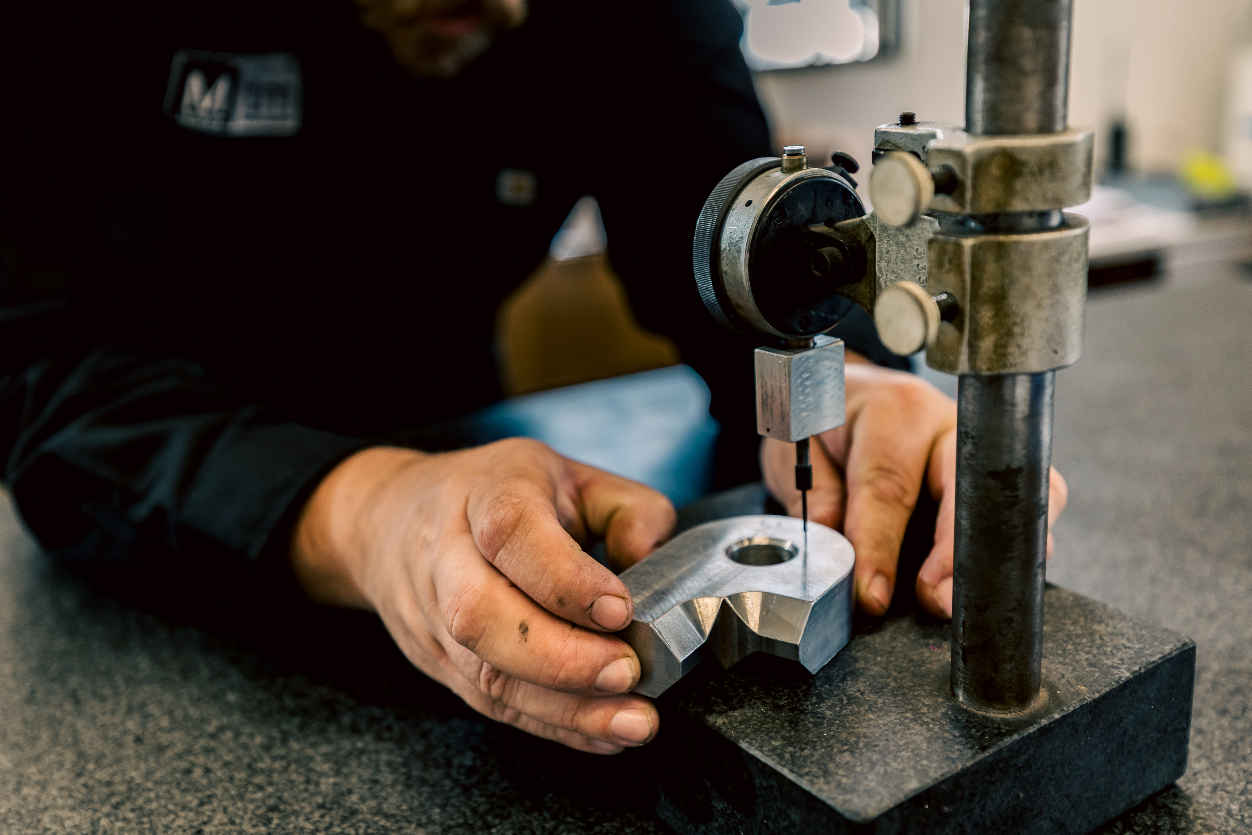 A close-up of a machinist's hands using a dial indicator to inspect a metal part before it goes to welding.