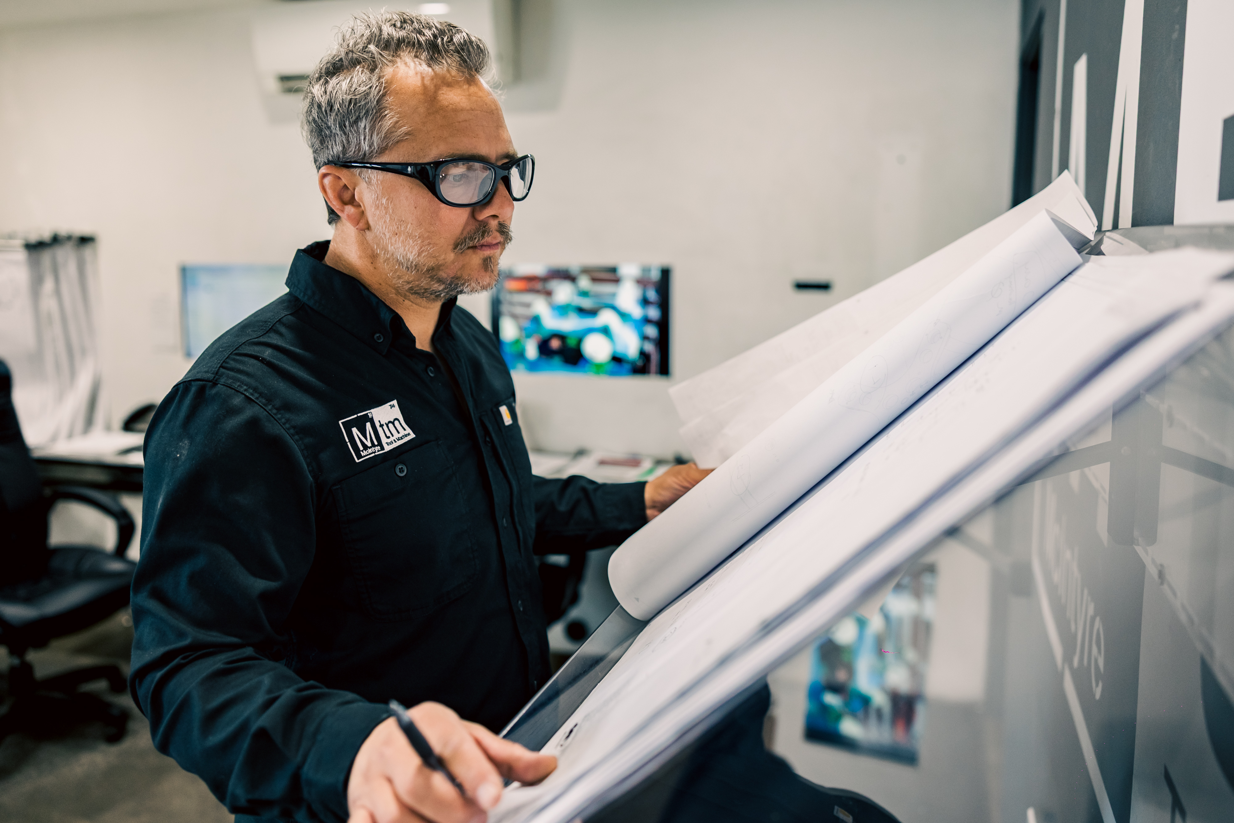 Dustin McIntyre is analyzing engineering plans to prepare a quote for a new project in a professional office environment at MTM.