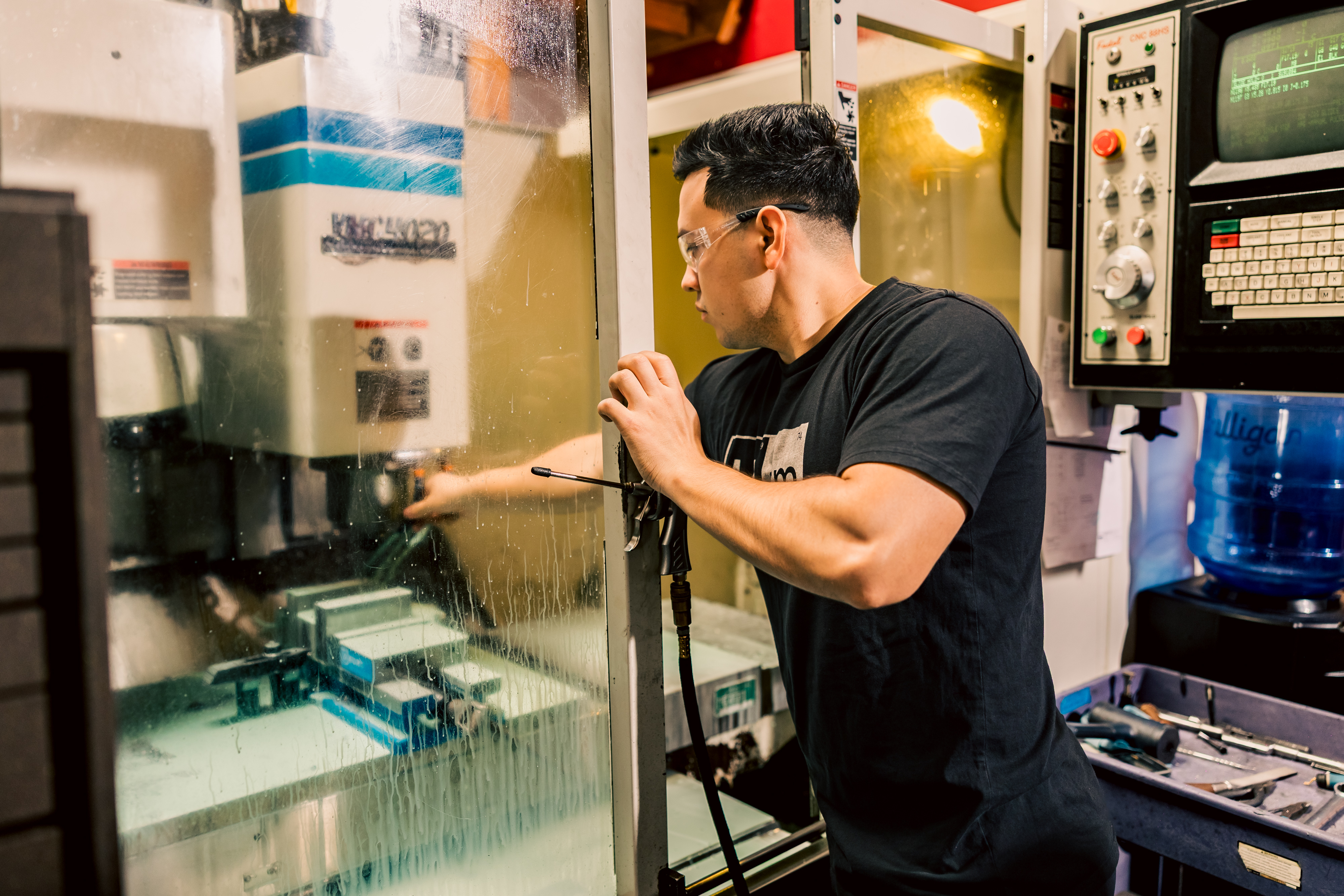 A machinist verifying coolant flow while a Fadal 4020 mills hardened steel in the workshop.