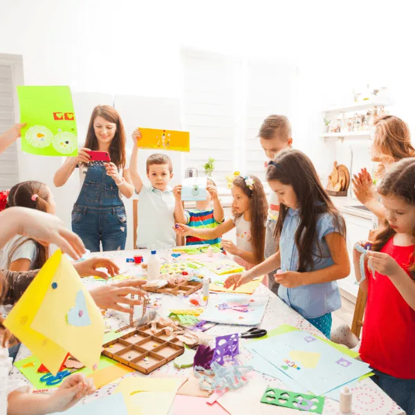 A group of happy children celebrating at a birthday party indoors, some wearing party hats.