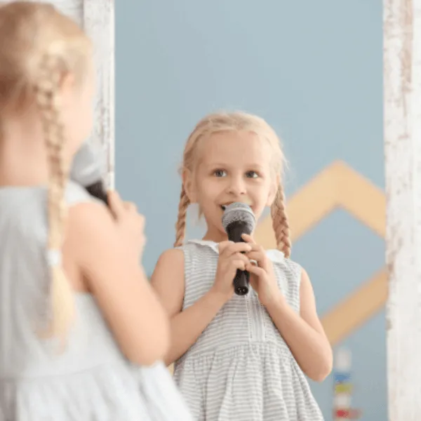 A young girl with blonde hair enthusiastically singing into a microphone.