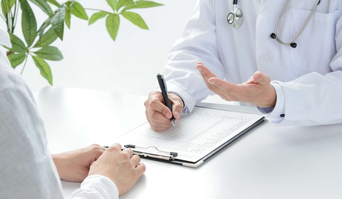 A close-up of two hands, one older and one younger, gently clasped over a table with soft natural light, symbolizing intergenerational support and community care. The background is softly blurred in warm neutral tones.