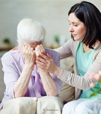 Elderly woman grieving with her hands at her face while a younger woman comforts her, symbolizing grief and bereavement support services.