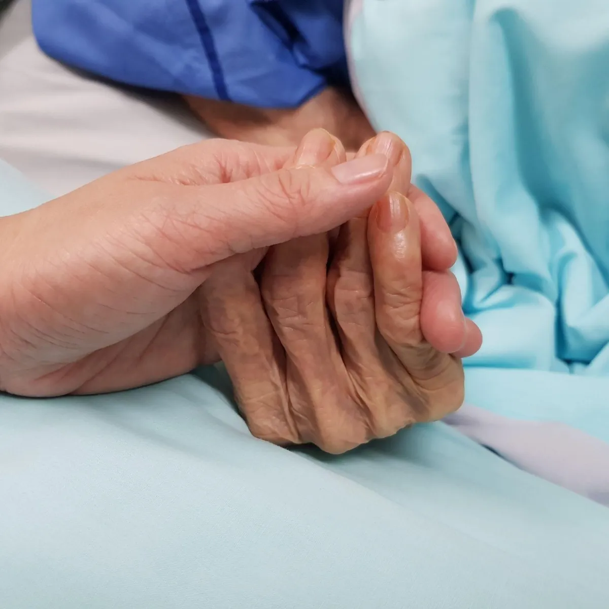 A young hand gently holding an elder person's hand, symbolizing grief coaching, end-of-life support, and emotional care for caregivers.