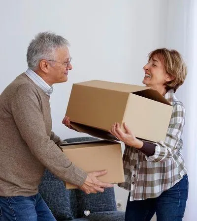 Elderly man and woman smiling as they pass off boxes, highlighting compassionate senior relocation services.