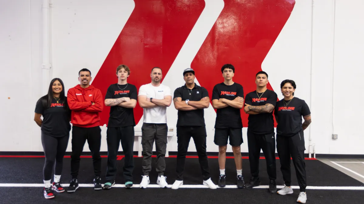 Redline Athletics Ventura Coaches stand and smile in front of Redline logo wall 