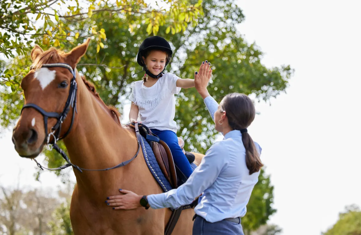 Child receiving a therapeutic horse riding lesson with gentle support and safety equipment