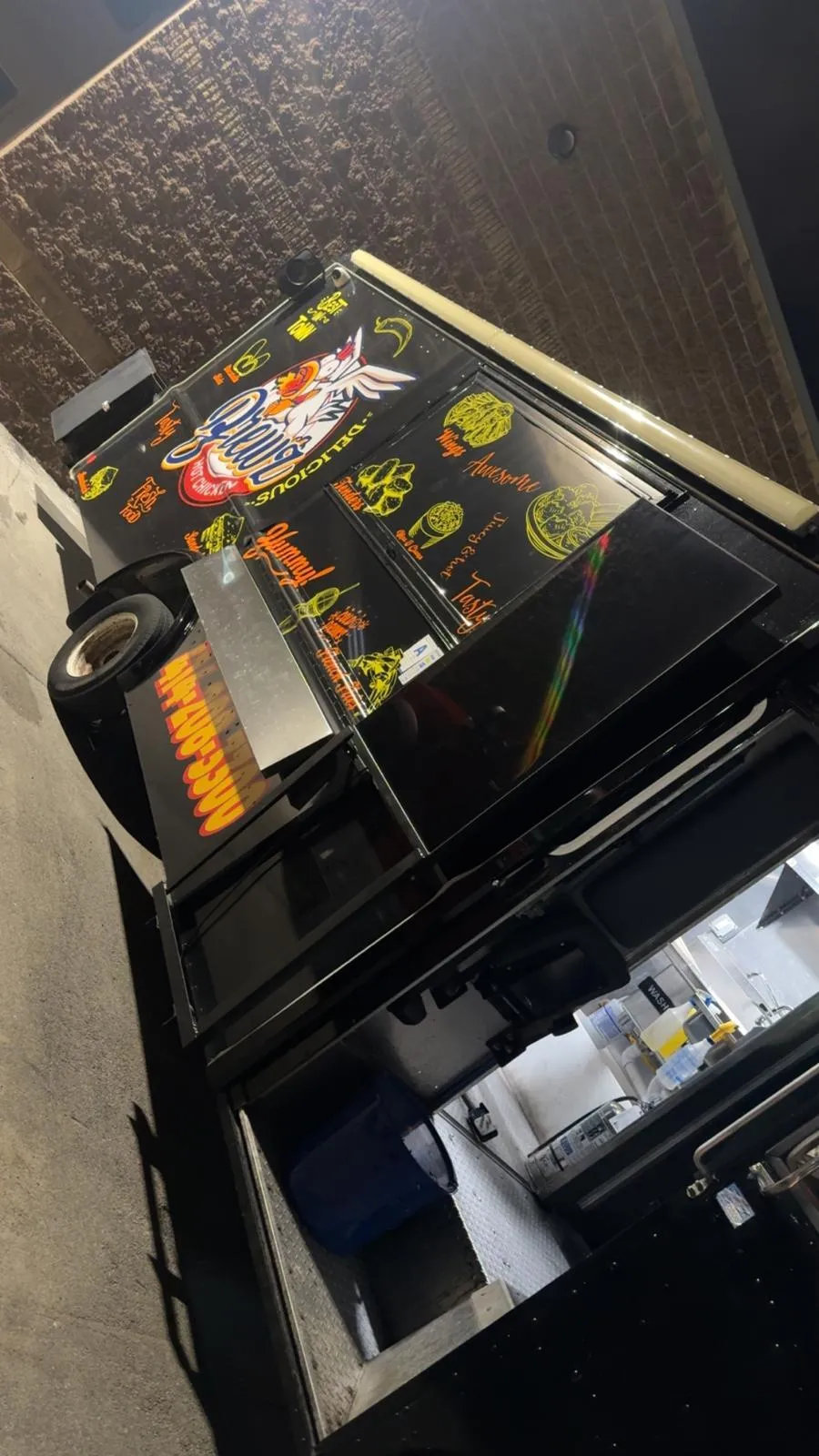A 3:2 image showing the exterior of Brewz Hot Chicken restaurant, with a bold red and yellow sign, large windows, and a welcoming entrance. The scene includes a diverse group of customers entering and leaving, set on a sunny day in a lively urban neighborhood.