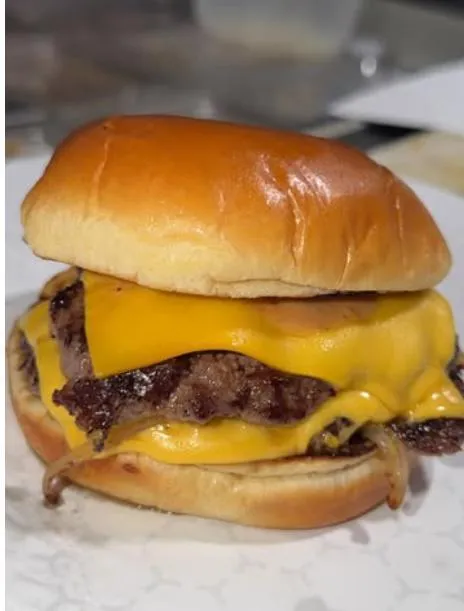 A 1:1 image of the Brewz Hot Chicken customer service team, featuring three friendly staff members of different backgrounds, smiling at a counter with a bright, modern interior behind them. The setting is casual and approachable, emphasizing hospitality and readiness to assist.