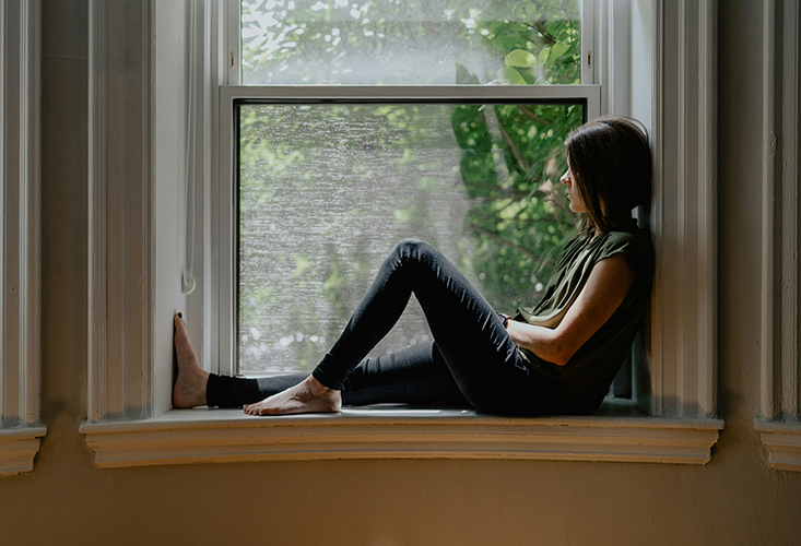 Woman sitting inside window sill.