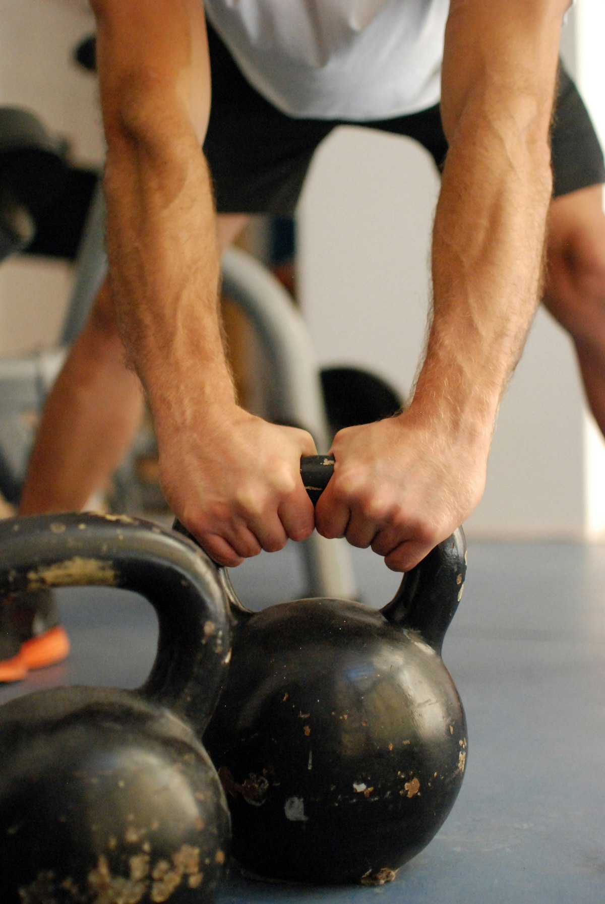 Close-up of a person's hands gripping a heavy kettlebell with both hands during a strength training session in a gym